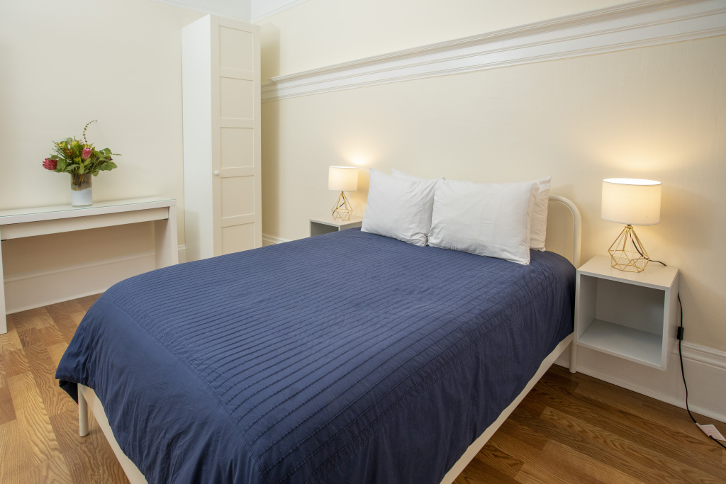 A neatly made bed with a blue cover in a room with white furniture and decor.