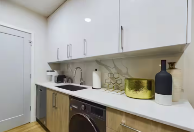 Admire the elegant details of this kitchen, featuring a stunning quartz waterfall backsplash and sleek white countertops. The warm wood cabinetry and modern hardware create a refined, minimalist aesthetic, perfect for both style and function.