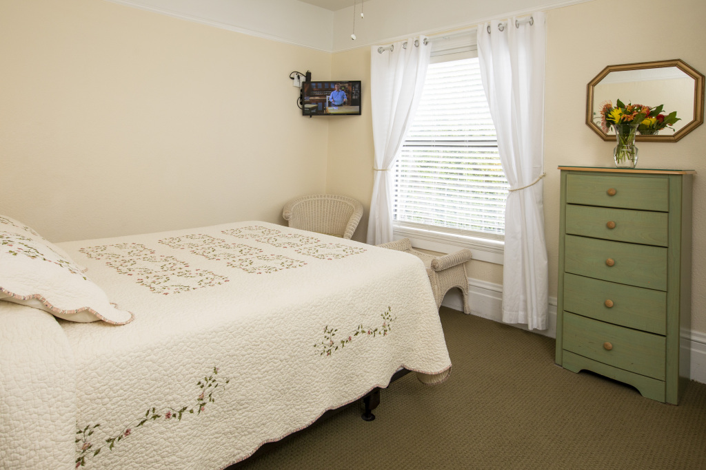 A hotel room with a bed, dresser, window, TV, and chair.