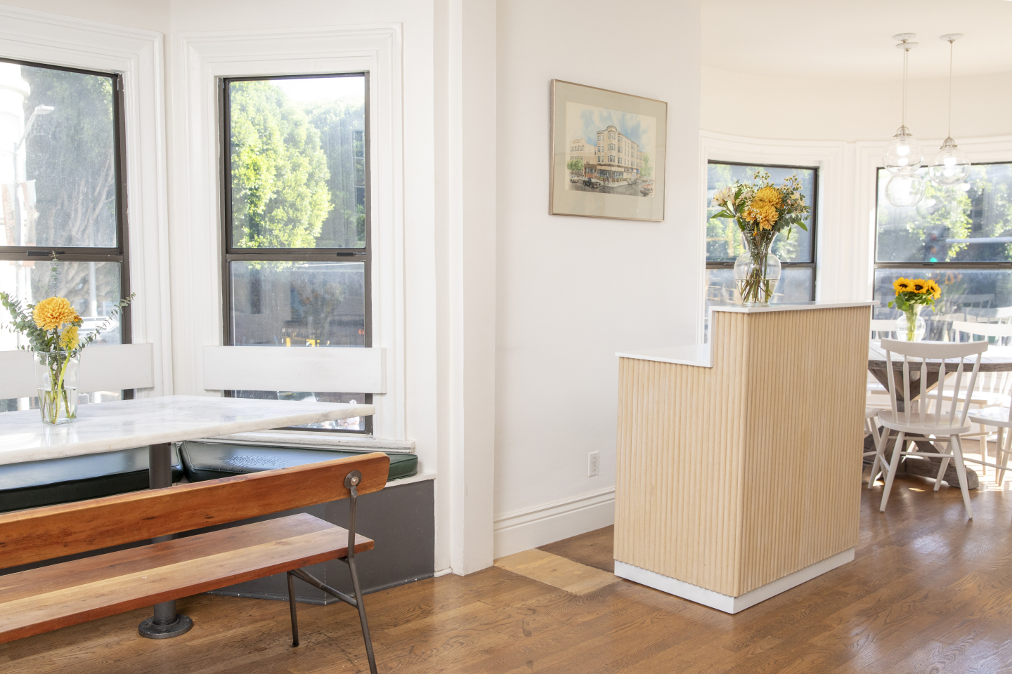 A bright and airy lobby with white walls, wooden floors, and a bench and table with flowers.