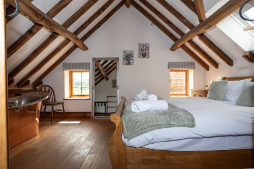 Beautifully presented bedroom with high beams, night-lit windows, hotel-crisp linens and a luxurious copper bath