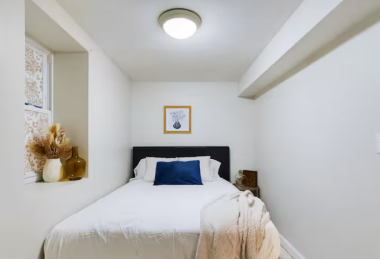 Unwind in this serene retreat featuring a plush queen bed with crisp linens and a cozy throw. A charming window nook adds a decorative touch, while soft lighting and modern decor create a relaxing ambiance for restful nights.