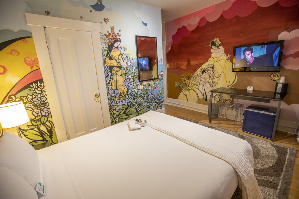 A hotel room with a large bed, a TV mounted on the wall, and a desk with a chair.