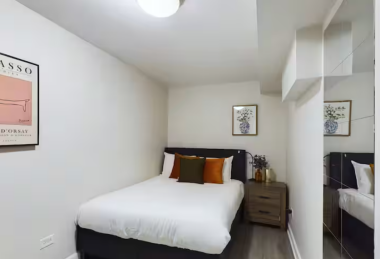 Relax in this modern, stylish bedroom featuring a comfortable double bed with vibrant accent pillows. A sleek mirrored wardrobe, elegant decor, and soft lighting create a chic and inviting space for your stay.