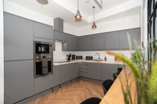 A spacious, modern kitchen fully equipped with integrated appliances, breakfast seating, and complimentary tea, coffee and sugar - perfect for gathering with friends or family during your Birmingham stay.