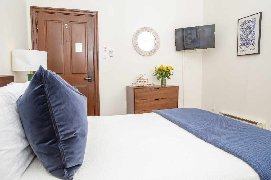 A neatly arranged hotel room with a bed, TV, lamp, mirror, and dresser.