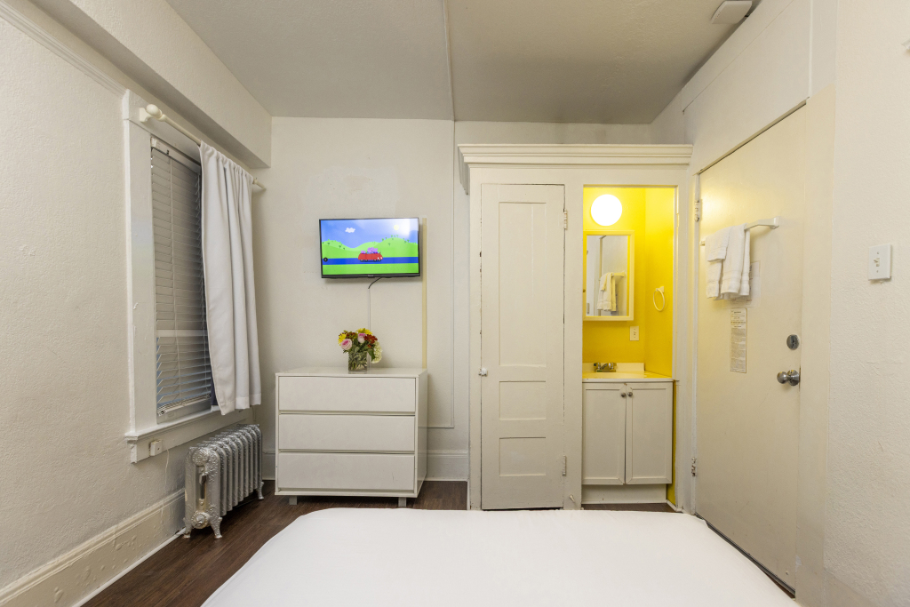 A wide view of a hotel room with a bed, TV, dresser, and bathroom door open.