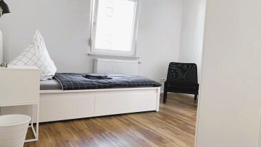 Helle Einzelzimmer mit funktionaler Ausstattung: Bett, Schrank und Sitzgelegenheit – ideal für längere Aufenthalte mit Privatsphäre.