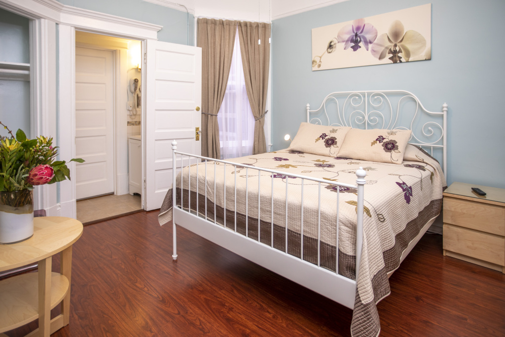 A wide view of a hotel room with a white metal bed, floral bedding, and light blue walls.