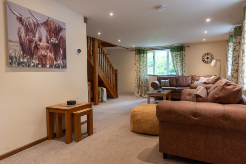 Spacious Open-Plan Living Room - Generous seating for the whole group, original staircase and charming Highland cow family artwork — with the 80-inch Smart TV just through the nook (inside complete with ample board games)