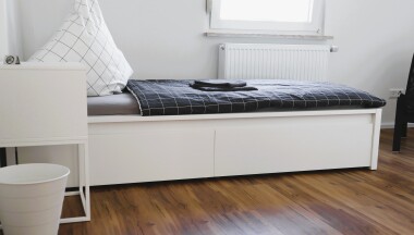 Helle Einzelzimmer mit funktionaler Ausstattung: Bett, Schrank und Sitzgelegenheit – ideal für längere Aufenthalte mit Privatsphäre.