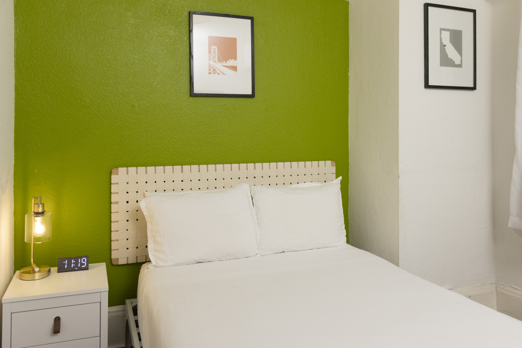 A neatly made bed with white bedding and pillows against a green accent wall in a hotel room.