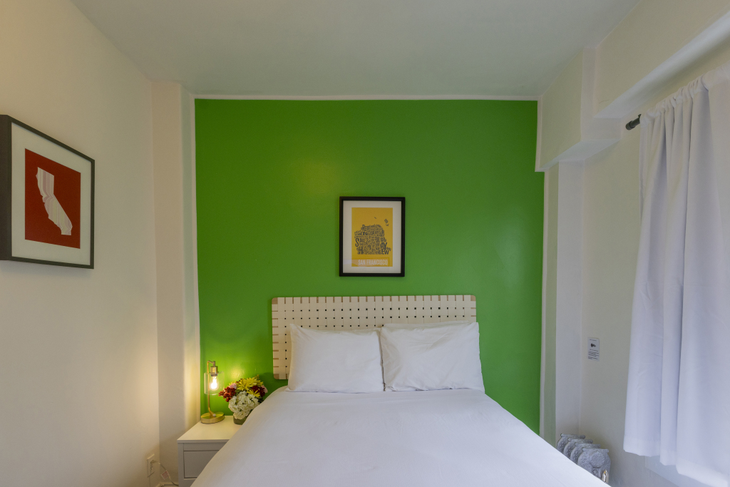 A hotel room with a green accent wall, a white bed, and a nightstand.