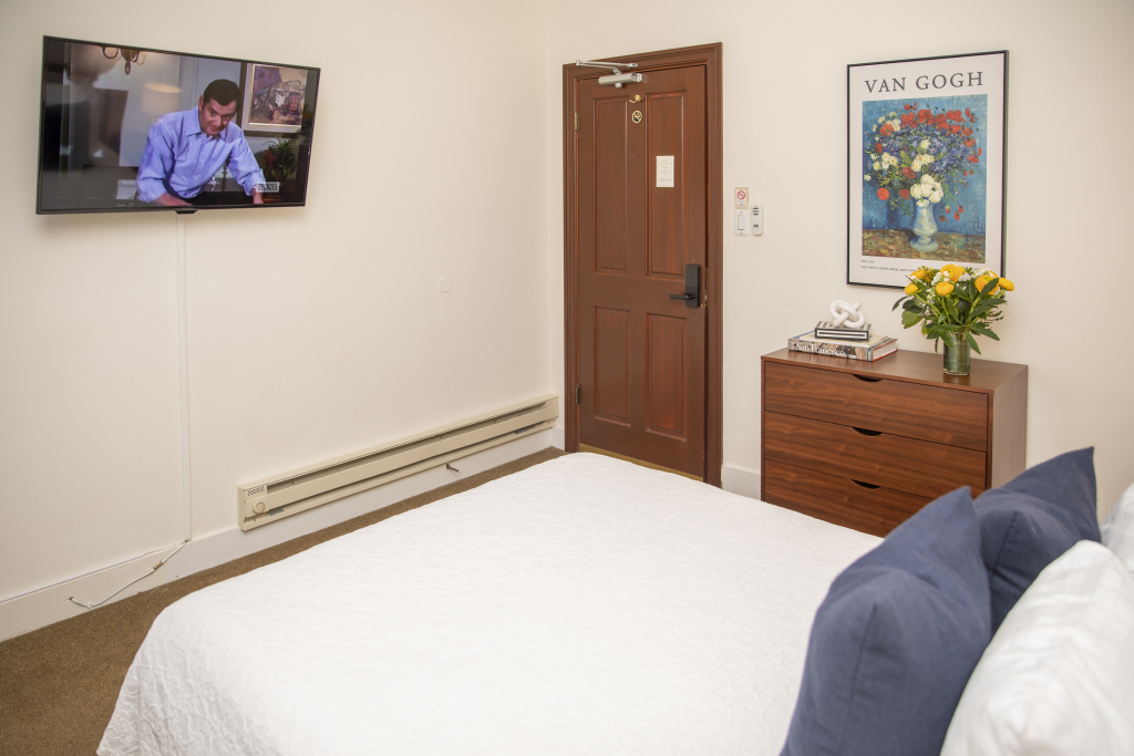 A hotel room with a bed, TV, dresser, and door.