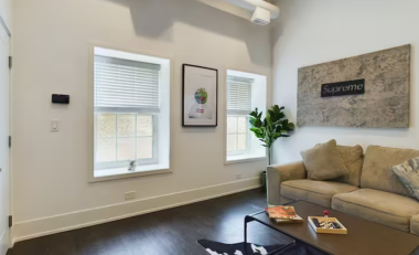 Step into this stylish living room with bright windows, trendy framed art, & a bold Supreme wall decor. A lush green plant adds life to the space, while the sleek center table & rich wooden flooring complete the perfect blend of comfort & modernity.