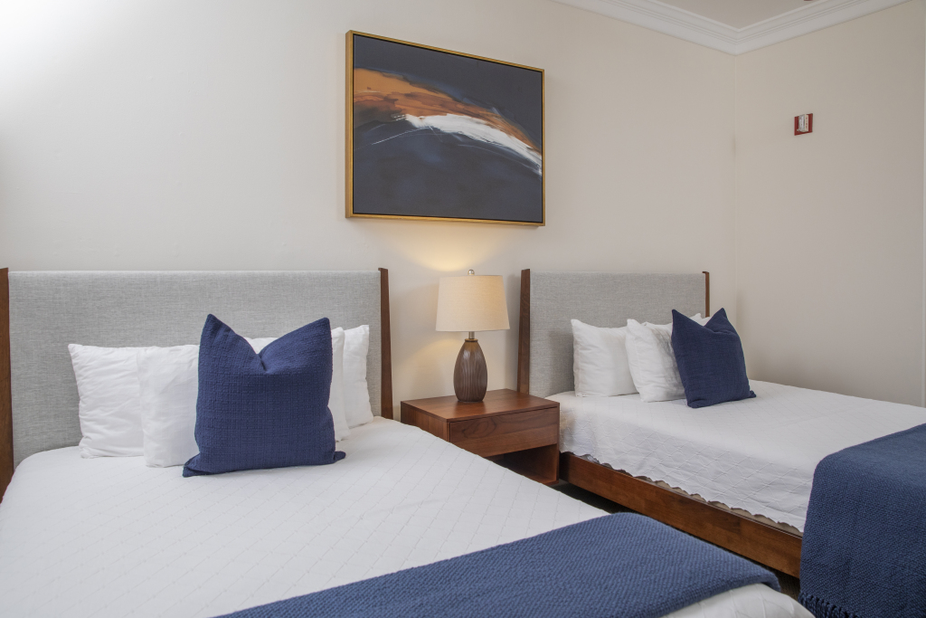 A hotel room with two beds, a nightstand, and a painting on the wall.