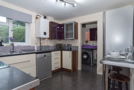 A tastefully decorated modern kitchen with integrated appliances including an oven and dishwasher, plus a large fridge freezer, coffee maker, toaster and washing machine. A breakfast bar with stools provides additional seating and a handy workspace.