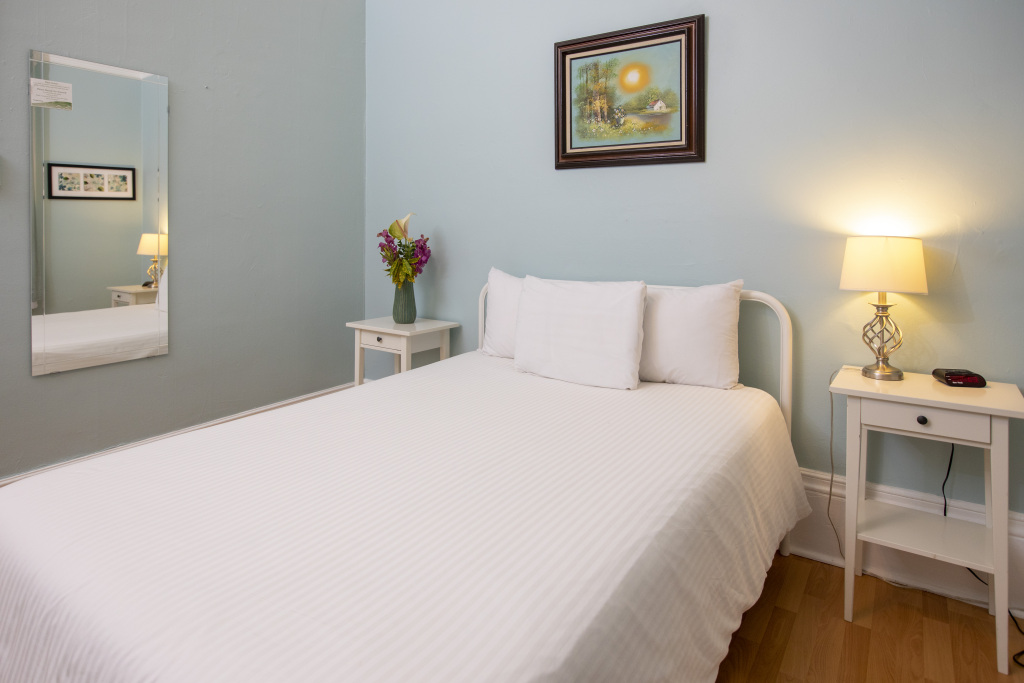 A neatly made bed with white linens and pillows, flanked by two nightstands with lamps, in a room with light blue walls and a mirror.