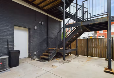 This exterior space features a sturdy black metal staircase, a private fenced area, and durable concrete flooring. The modern industrial design adds character, offering convenient access and a secure outdoor space for practicality and functionality.