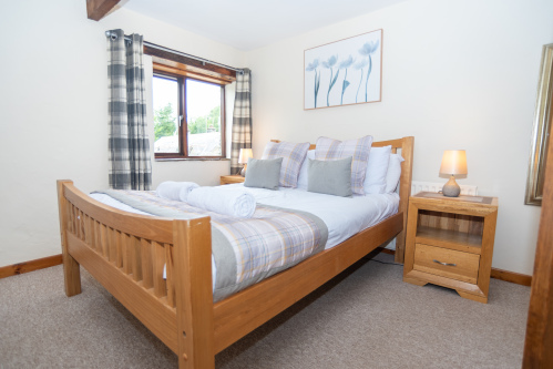 Light-filled master bedroom featuring a comfortable king-size bed, luxury linens and peaceful countryside views - perfect for a restful Devon escape.