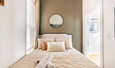 The main bedroom features a cozy queen bed bathed in natural light from the window, offering a serene and elegant space for restful and comfortable nights.
