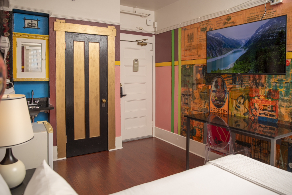 A colorful hotel room with a large flat screen TV, a desk, and a bed.
