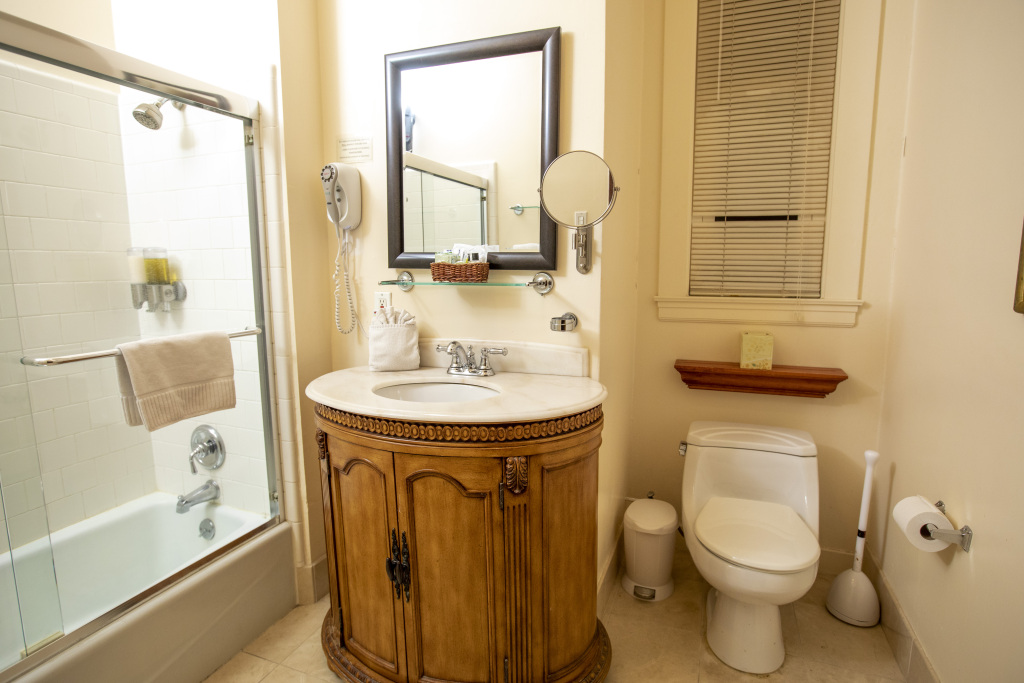 A standard bathroom with a shower/bathtub, marble sink, wooden cabinet, toilet, and mirror.