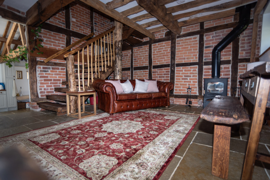Cosy living space with sofa, chairs, TV, log burner and a dedicated desk — all framed by a stunning handcrafted staircase