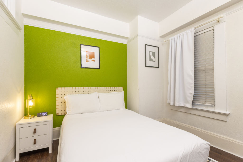 A hotel room with a white bed, green accent wall, and window.