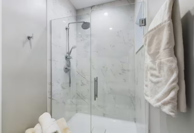 This full bathroom features a sleek glass-enclosed shower with modern chrome fixtures and elegant marble-inspired tiles. Plush white towels add a touch of luxury, making this space perfect for relaxation and rejuvenation.