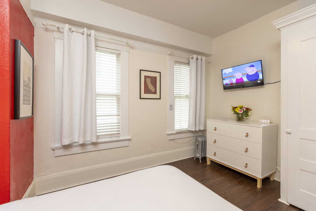 A hotel room with a bed, dresser, TV, and windows