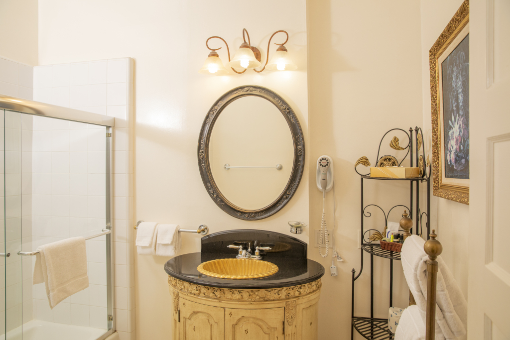 A bathroom with a black countertop, yellow sink, and ornate mirror