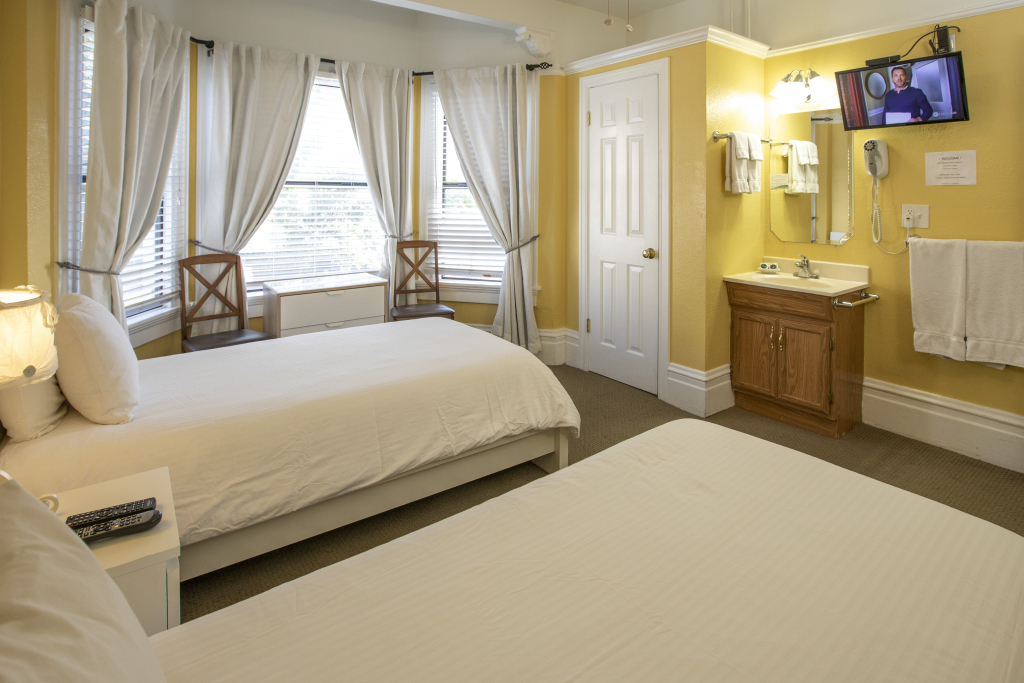 A hotel room with twin beds, a TV, sink, and window with curtains