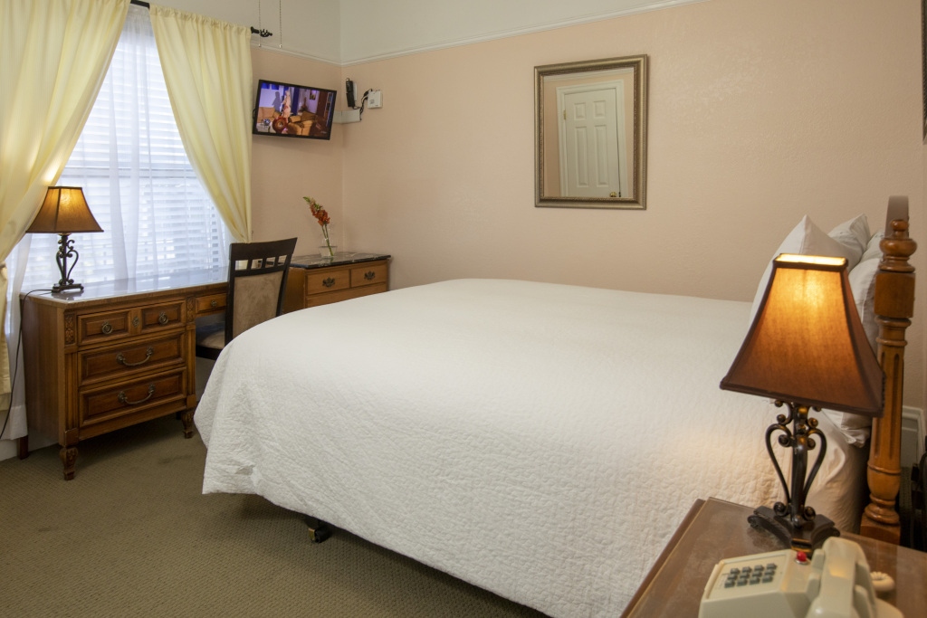 A wide view of a hotel room with a large bed, dresser, TV, and window.