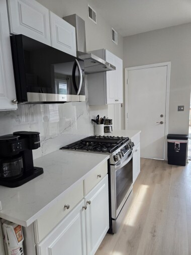 Discover the other side of this spacious kitchen, featuring a gas range, stainless steel hood, microwave, and coffee maker. Ample cabinet storage, marble-like backsplash, and sleek countertops make cooking a breeze, with easy access to other spaces.
