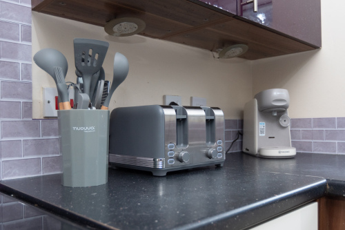 A tastefully decorated modern kitchen with integrated appliances including an oven and dishwasher, plus a large fridge freezer, coffee maker, toaster and washing machine. A breakfast bar with stools provides additional seating and a handy workspace.