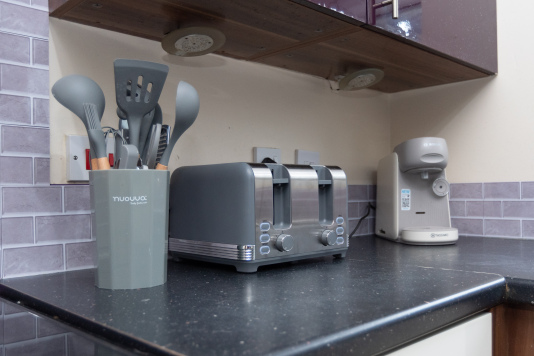 A tastefully decorated modern kitchen with integrated appliances including an oven and dishwasher, plus a large fridge freezer, coffee maker, toaster and washing machine. A breakfast bar with stools provides additional seating and a handy workspace.