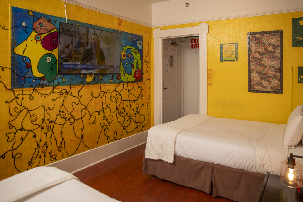 A room with yellow walls featuring abstract art, a double bed, and a doorway to another room.
