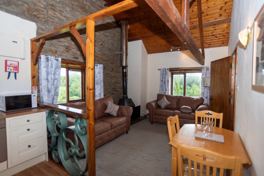 Characterful open-plan living space showcasing original mill features, exposed stonework, vaulted ceilings and cosy seating, with rolling countryside views covering every angle.