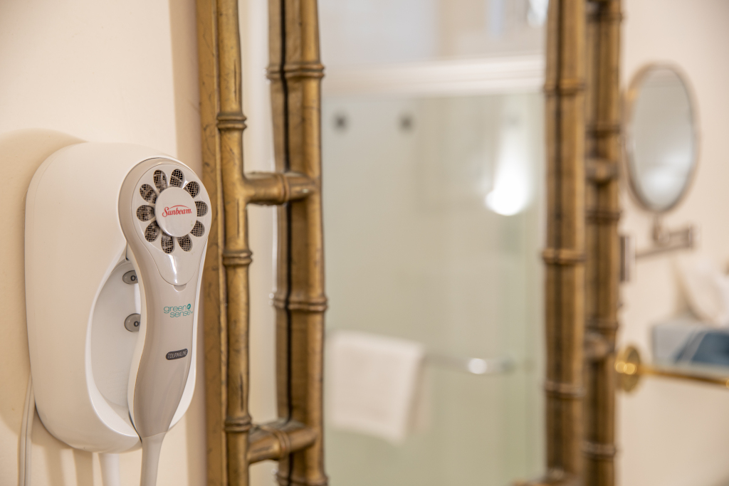 A close-up of a hair dryer next to a shower area with a glass door and mirror.