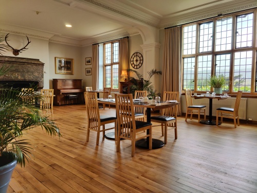 Breakfast room with many tables and chairs, and towering oak mullioned windows