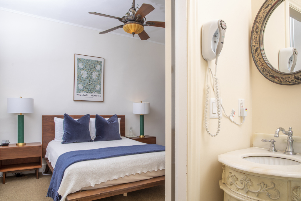 A hotel room with a bed, nightstands, lamps, a ceiling fan, and an adjoining bathroom with a sink and mirror.