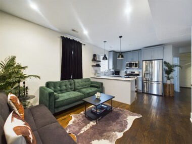 This stylish living area features a full-sized futon for lounging or extra sleeping space, a 50-inch TV for streaming, and chic bar seating. The cozy atmosphere, accented by a green feature wall, is perfect for relaxing or entertaining.