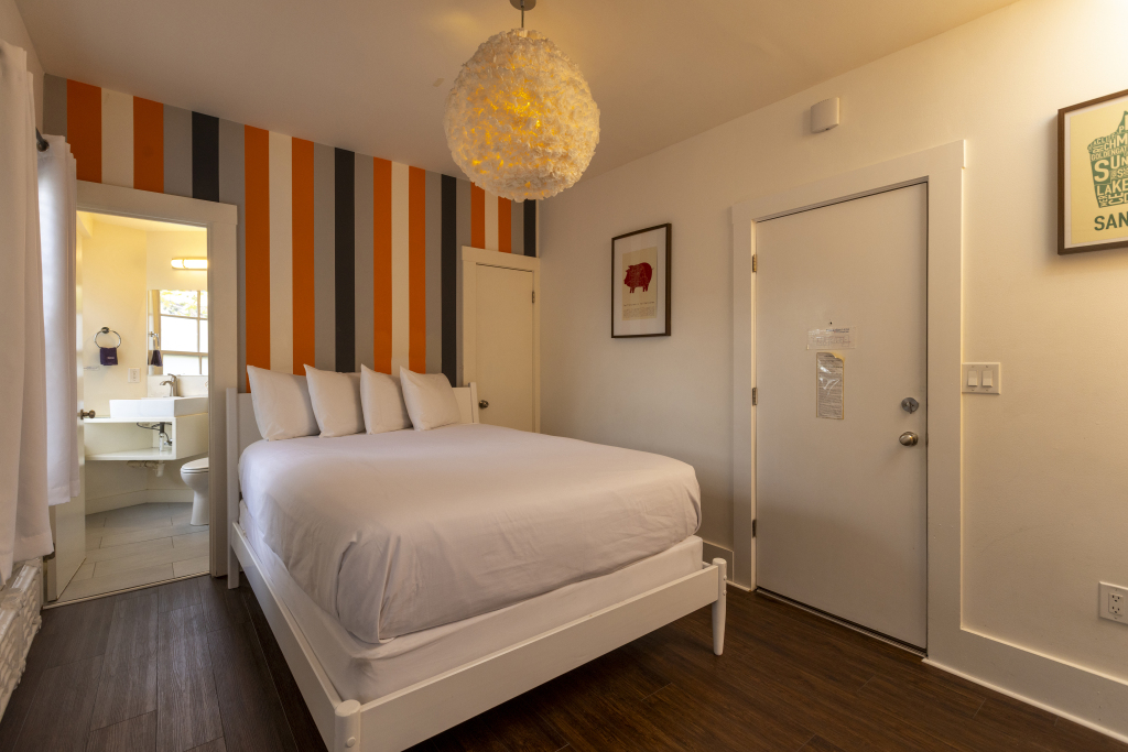 A hotel room with a white bed, bathroom, and modern light fixture.