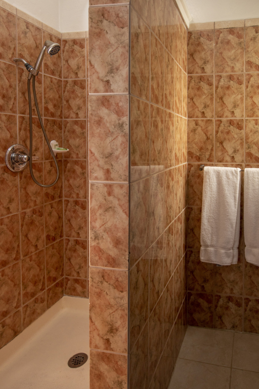 A shower area with tiled walls, a shower head, and two white towels hanging on a rack.