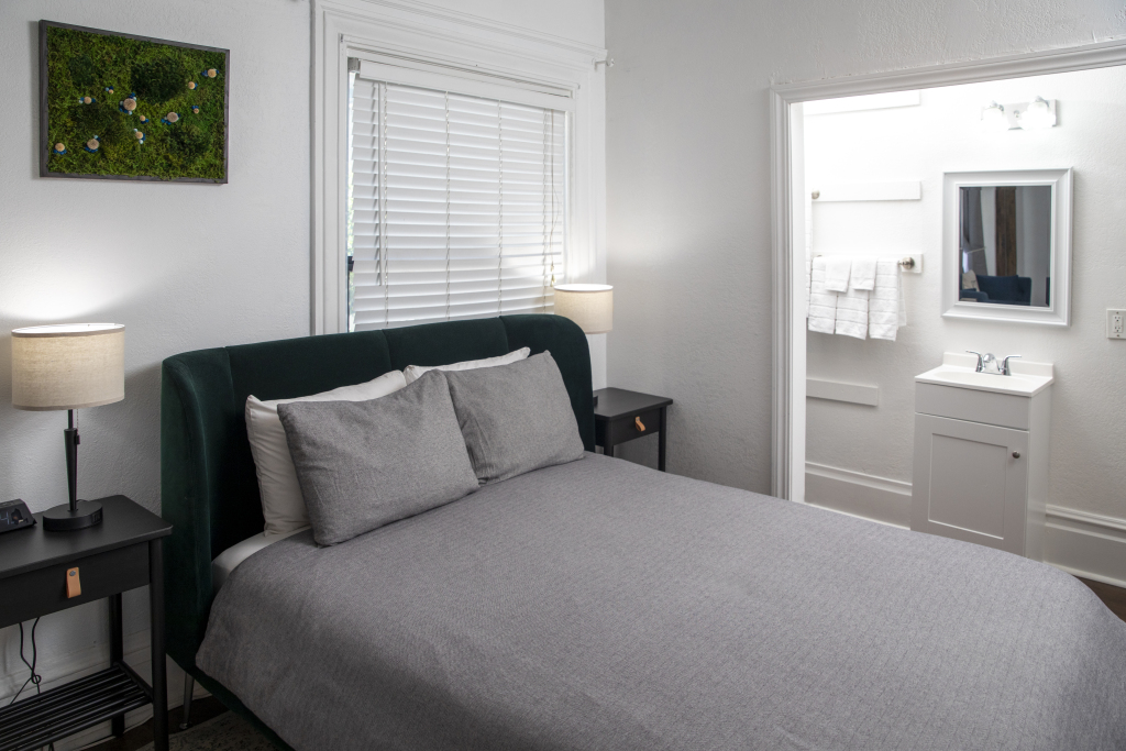 A hotel room with a bed, nightstands, lamps, a window, and a bathroom