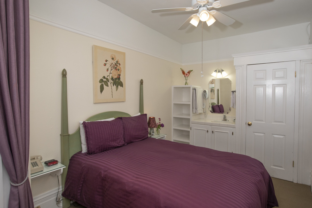 A hotel room with a purple bedspread, green headboard, and white furniture
