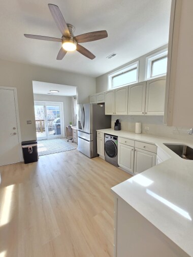 This modern kitchen boasts a sleek stainless steel French door fridge with a water dispenser, a built-in dishwasher, and an in-unit washer. Bright white cabinetry, elegant countertops, and natural light create a clean and welcoming space.