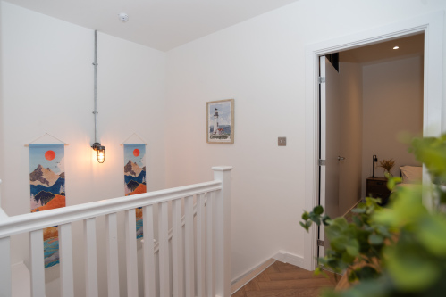 A bright hallway with stairwell leading downstairs to the remaining two bedrooms and the second bathroom.