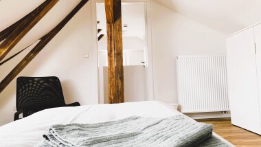 Helle Einzelzimmer mit funktionaler Ausstattung: Bett, Schrank und Sitzgelegenheit – ideal für längere Aufenthalte mit Privatsphäre.